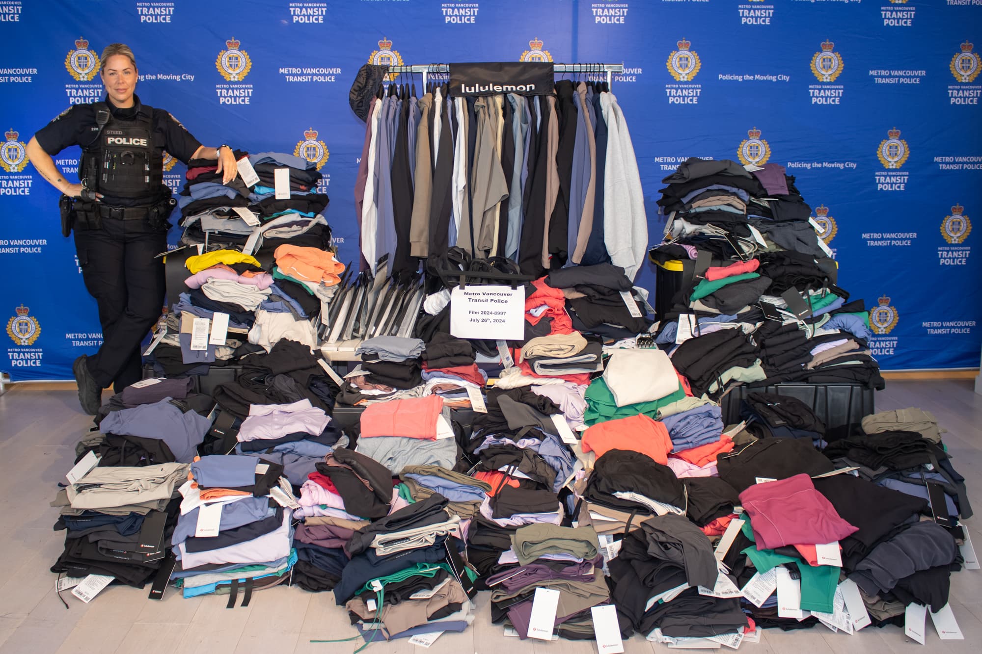 a police officers stands beside a very large stack of recovered clothing