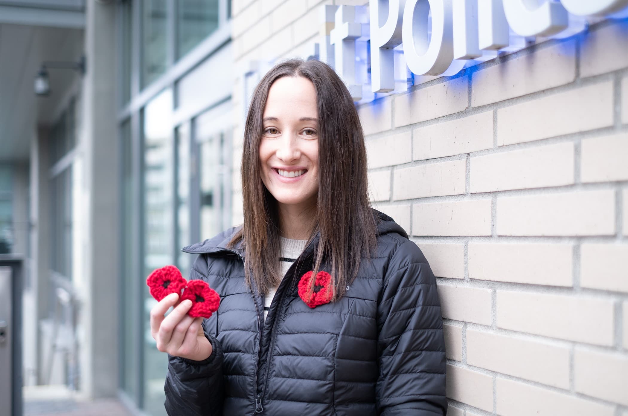 Alanna Wong stands outside Transit Police HQ wearing a hand-crocheted poppy and holding two others